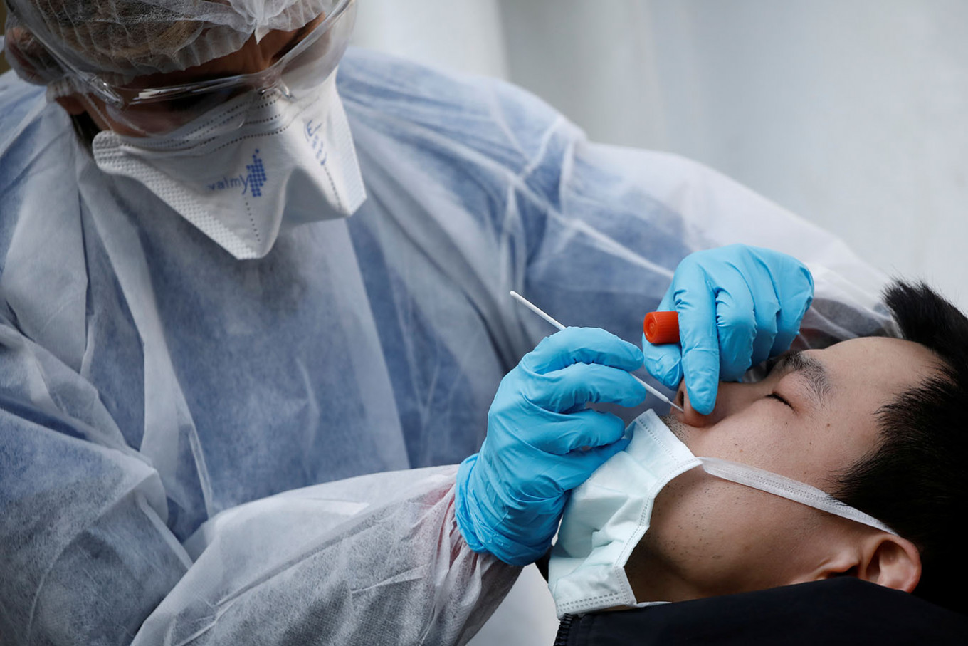 A medical biologist, wearing a protective suit, administers a nasal swab to a patient at a drive-through testing site for coronavirus disease (COVID-19) at the city hall of the 17th arrondissement in Paris as the spread of the coronavirus disease continues in France, March 27, 2020. (REUTERS/Benoit Tessier)